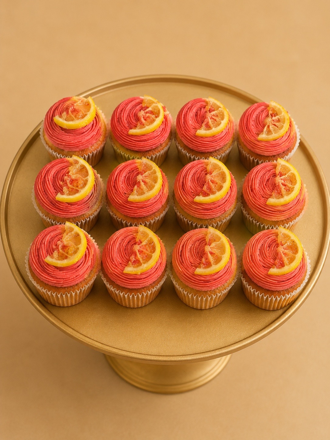 Tray of pink-frosted lemon drizzle cupcakes with candied lemon